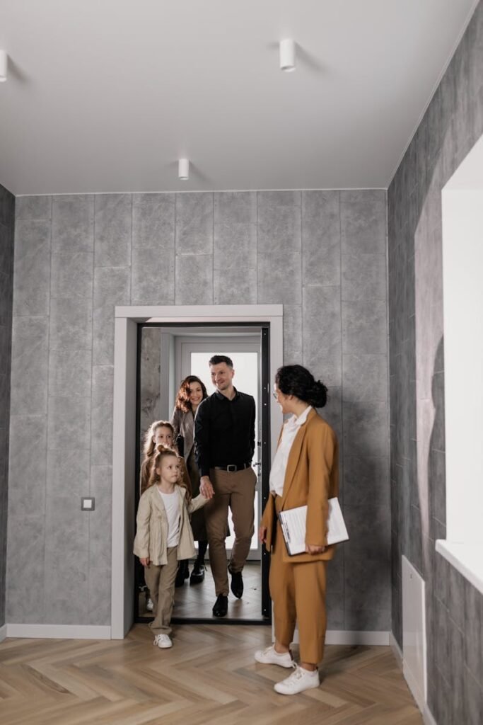 A family enters a new home with a real estate agent welcoming them inside.